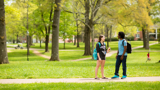 Two students chat on a sidewalk in the Quad.