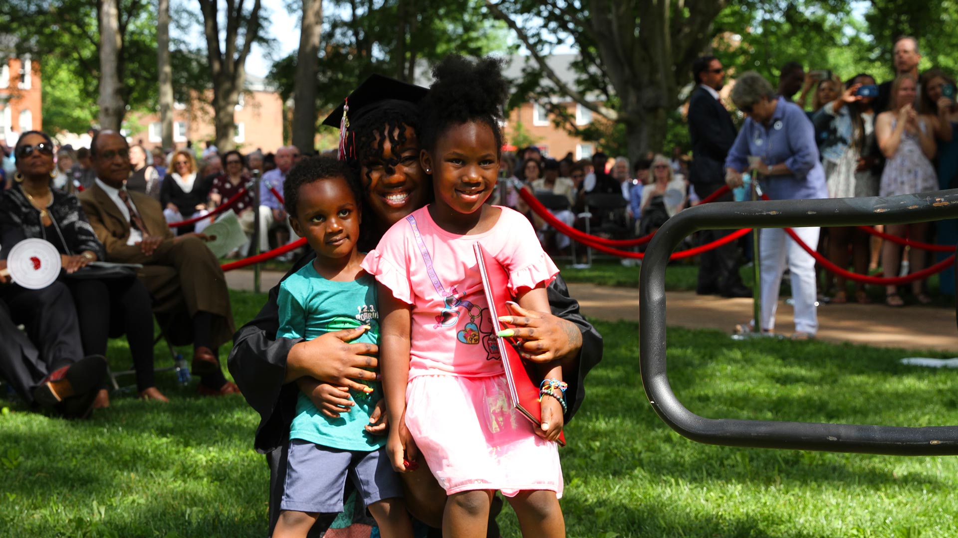 A student celebrates with small children after Commencement.
