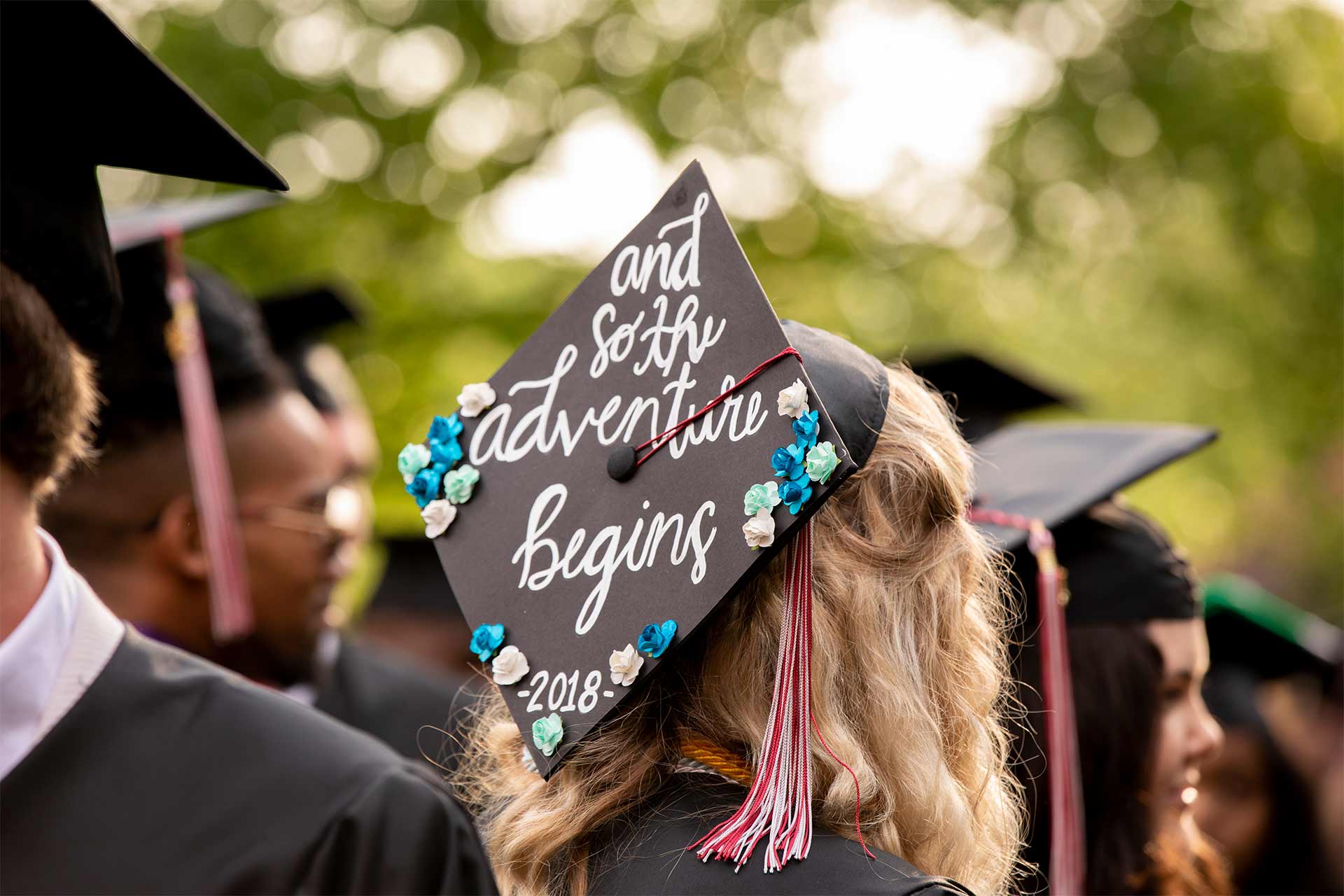 A student's mortarboard reads, "and so the adventure begins — 2018."
