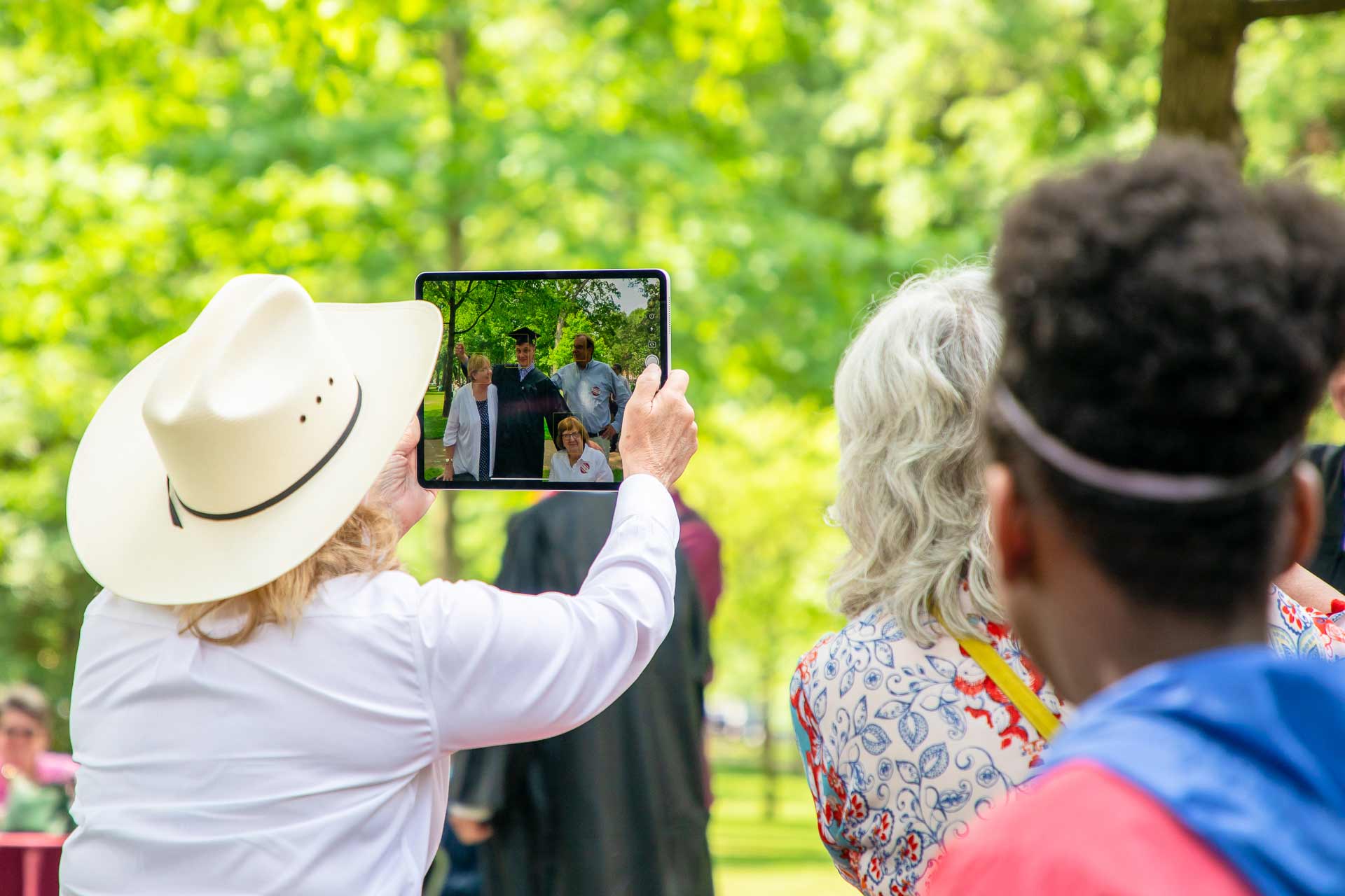 Friends and family take photos with a student using a tablet after Commencement.