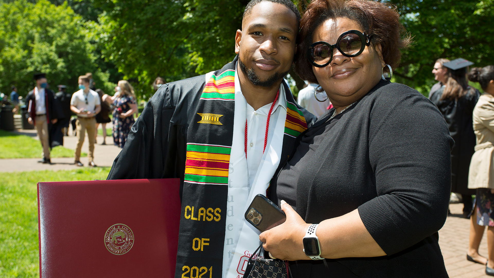 A graduate takes a photo with a friend while holding their new diploma.