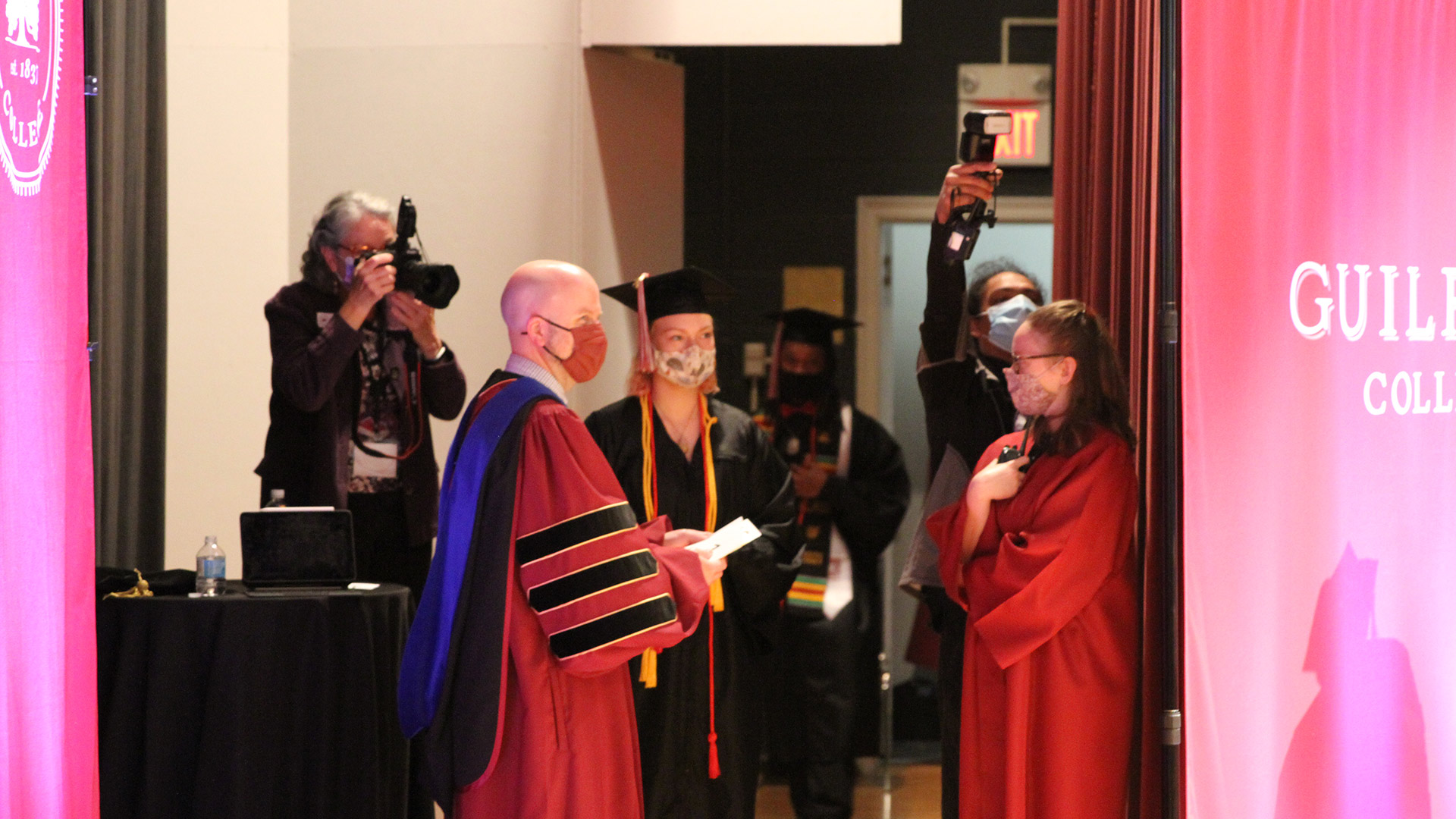 Students and faculty wait backstage as graduates stand in line waiting for their names to be called.