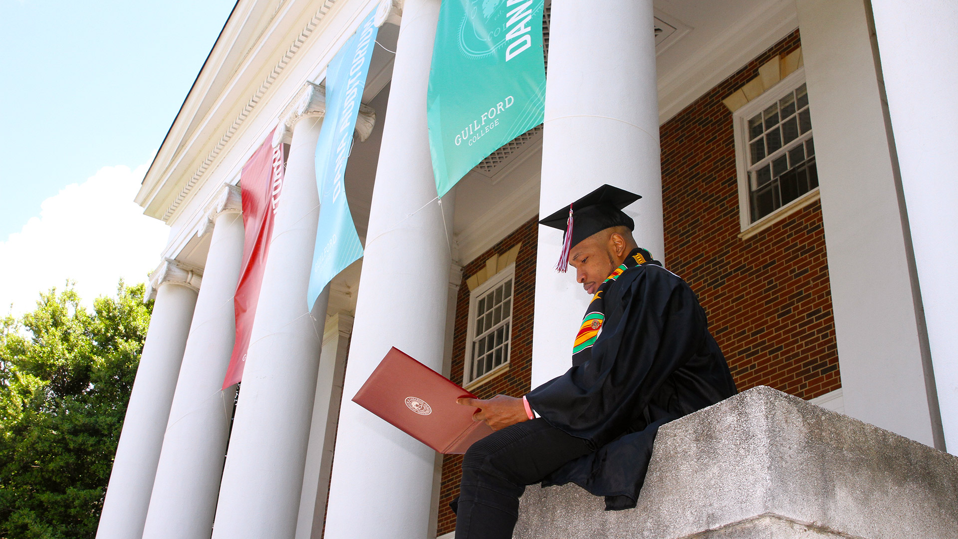 A student sits down to look at their diploma on the steps of Dana Auditorium.