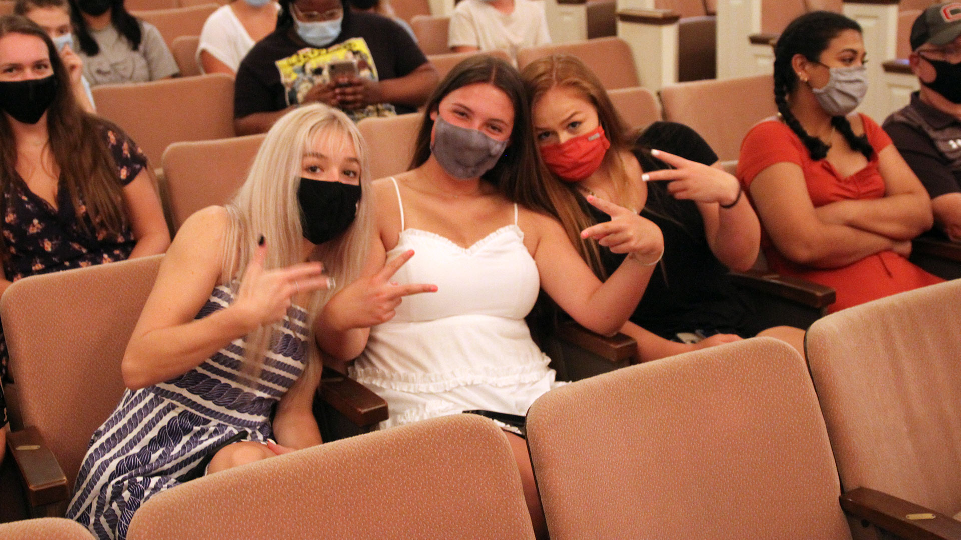 A group of three masked students show peace signs to the photographer.