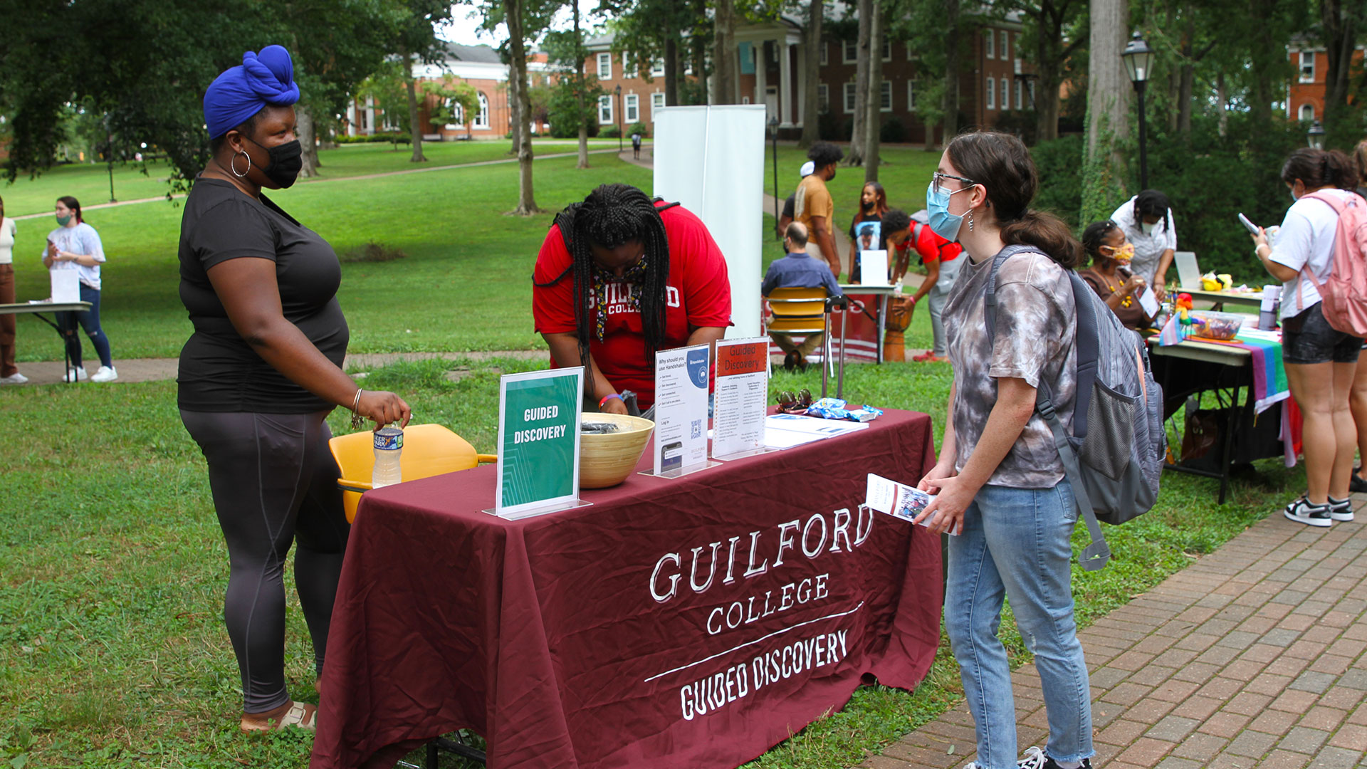 A student stops by the Guided Discovery table to chat with two Guilford Guides.