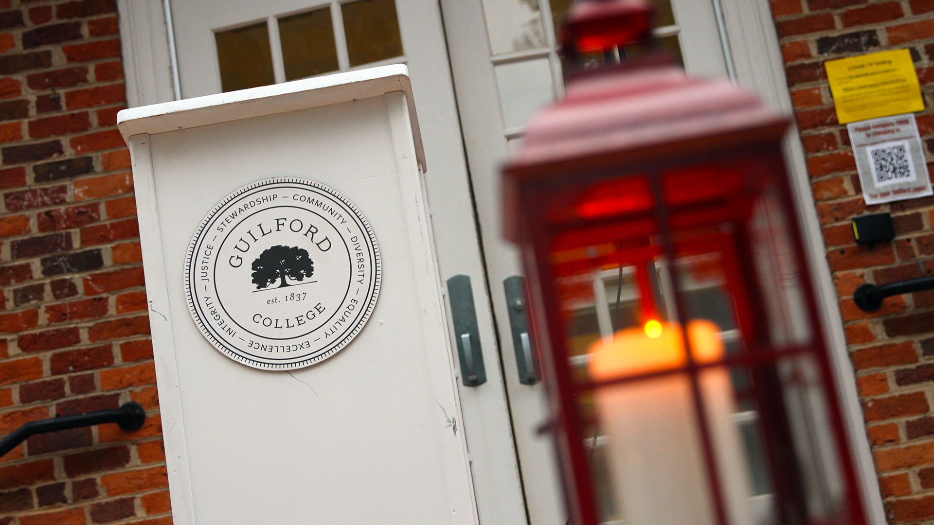 A red lantern with a lit candle inside sits next to a podium with the Guilford College emblem on it ahead of the Passing of the Light ceremony for new students.
