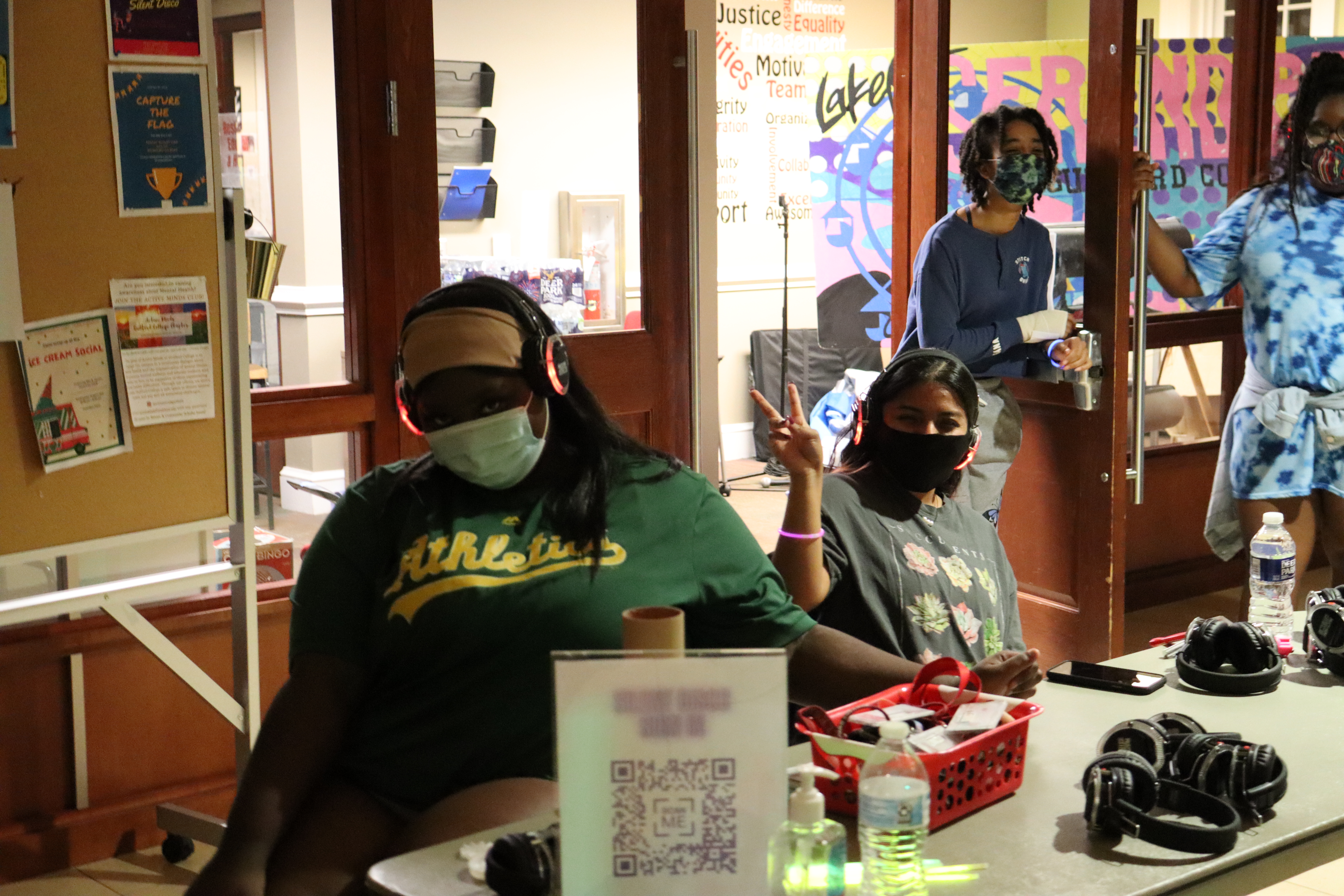 Students sit at a table in Founders Lobby, passing out headphones for the Silent Disco event.