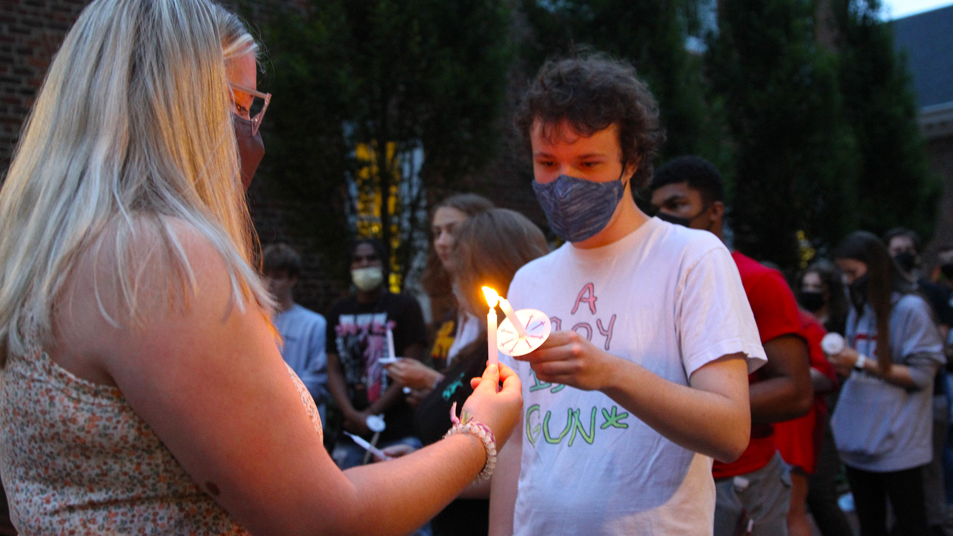 A student uses their candle flame to light another student's candle.