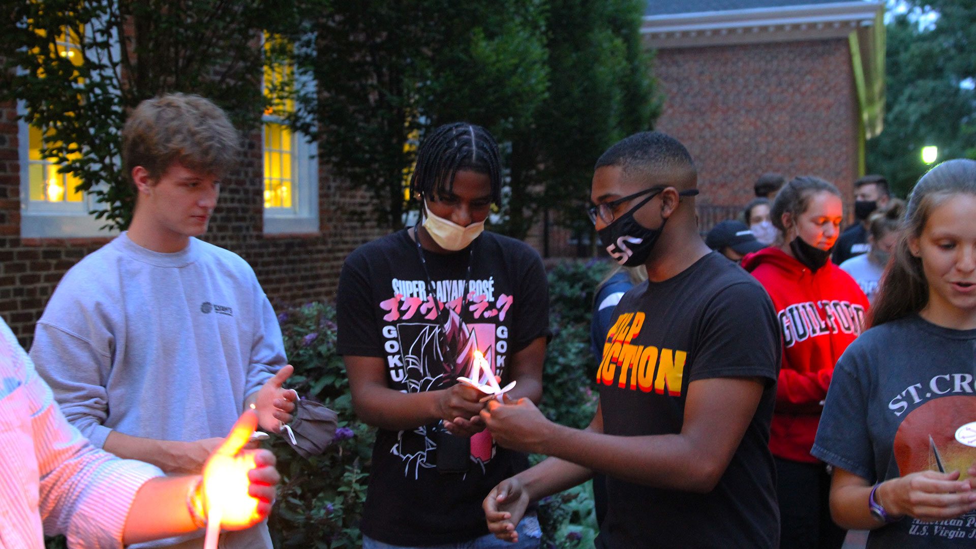 Students standing on Founders Patio pass their candle flame to one another.