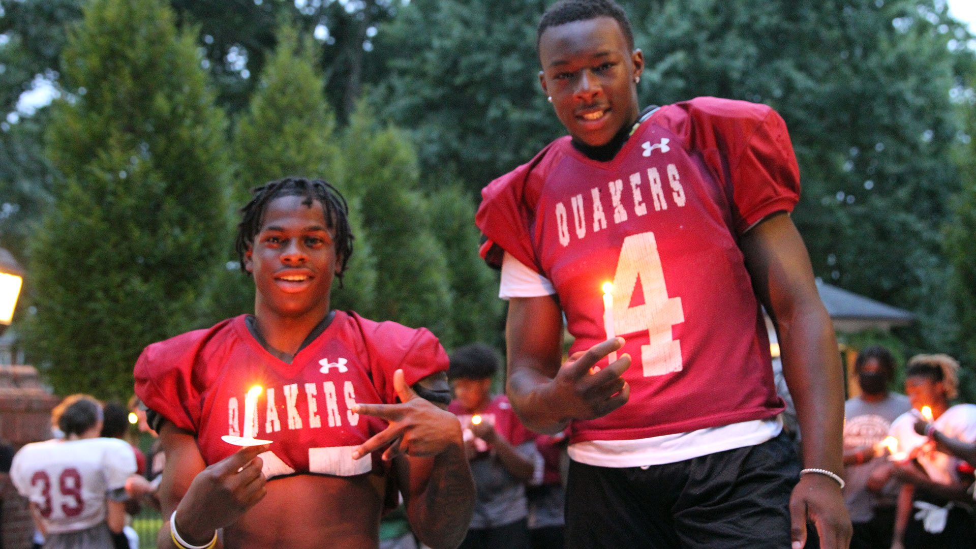 Two football players hold their candles and smile at the camera.