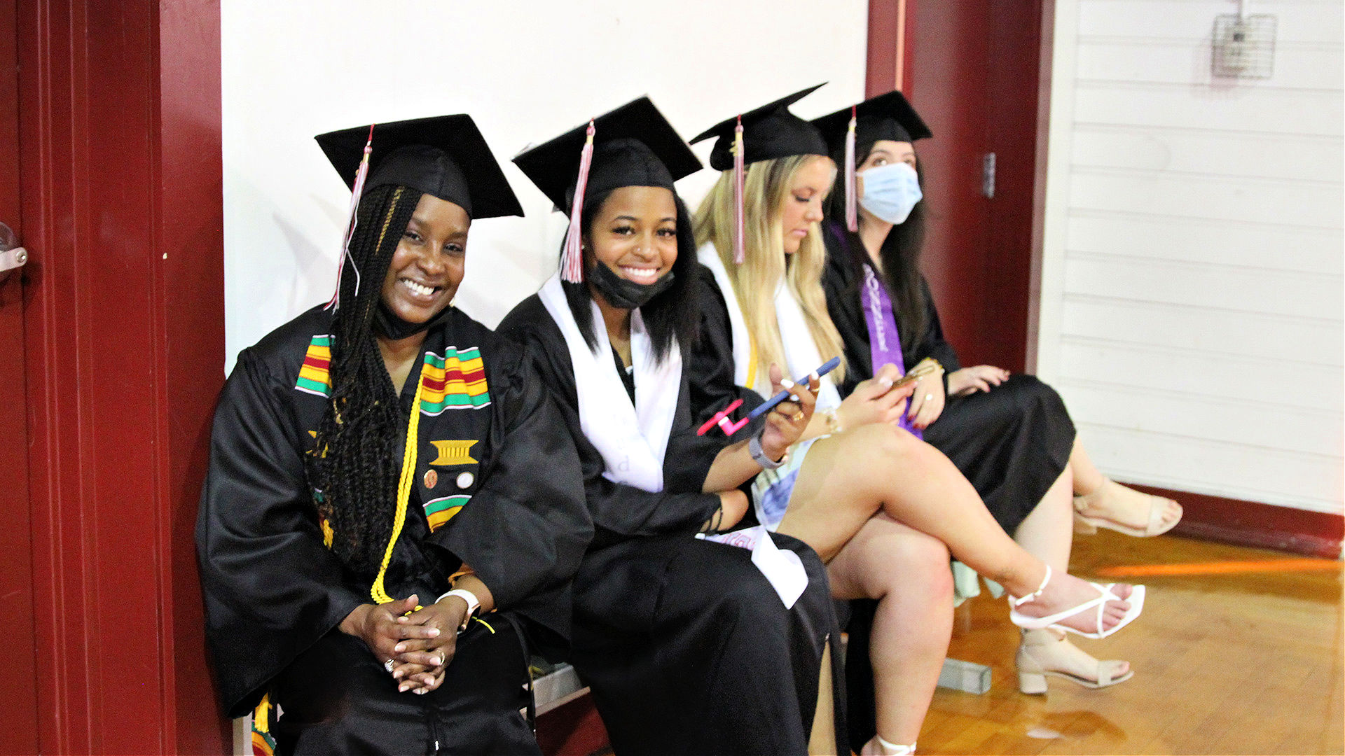 Four students sit on a bench, waiting for Commencement to begin.