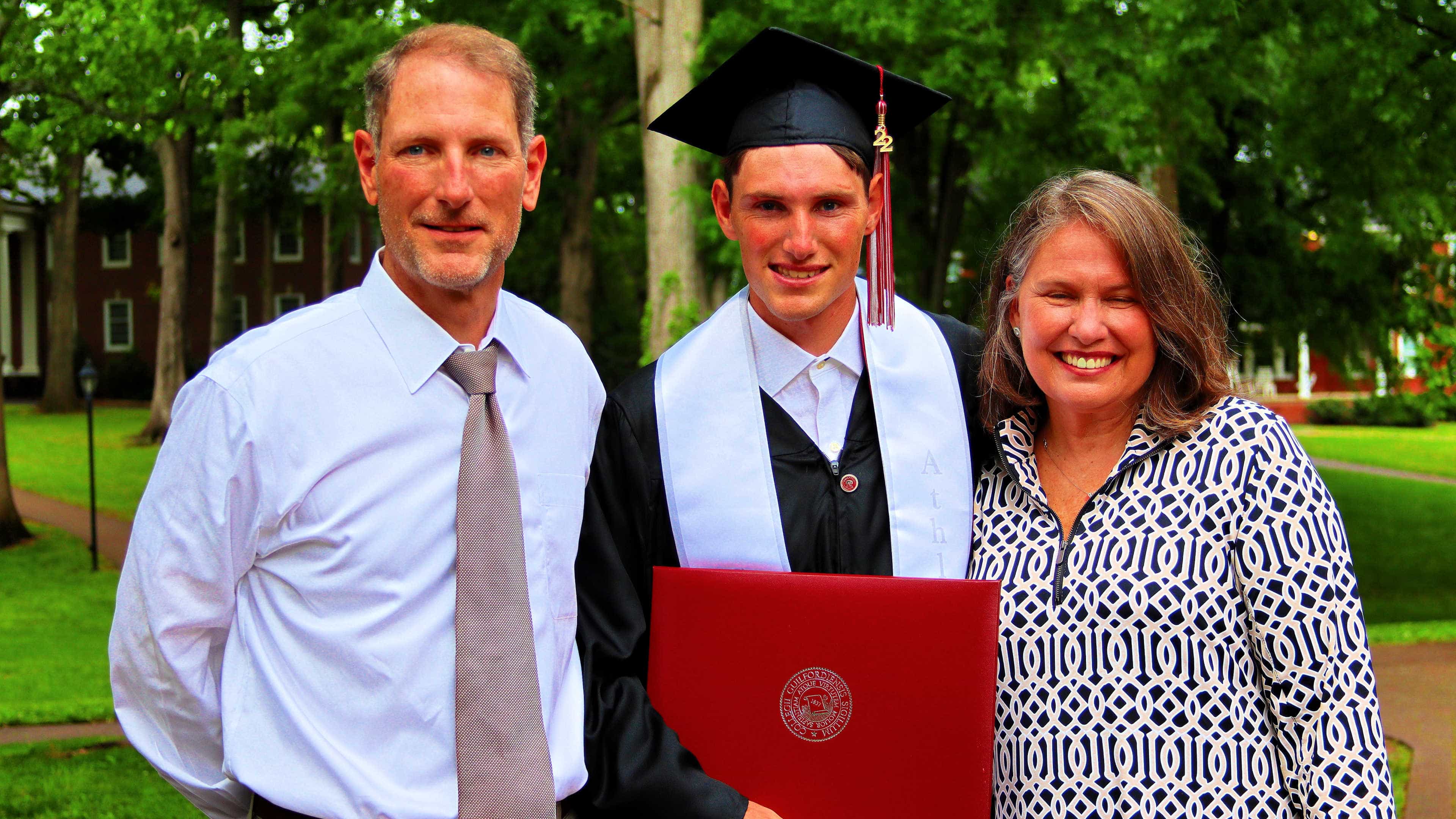 A student holding their diploma takes a photo with two family members..