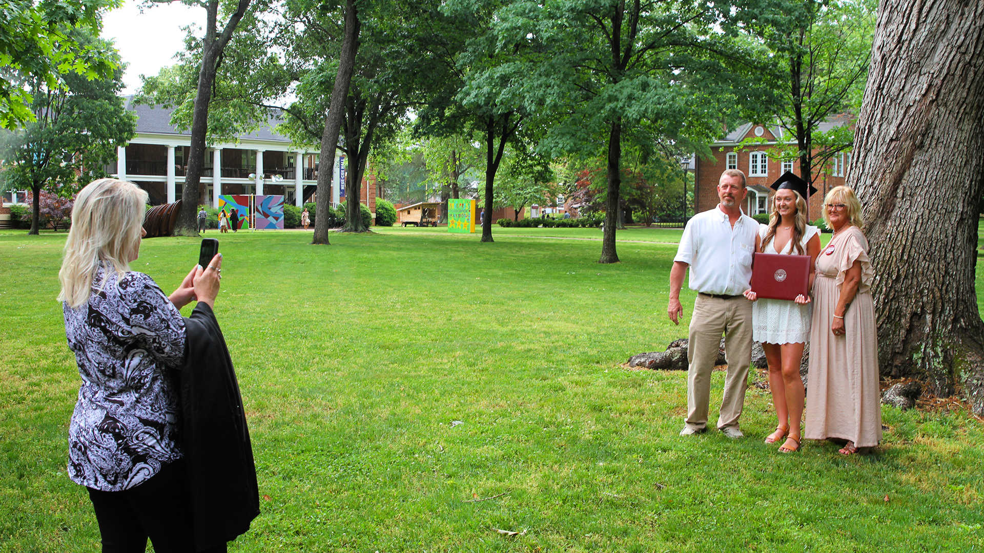 A friend takes a photo of a student outdoors with two family members.