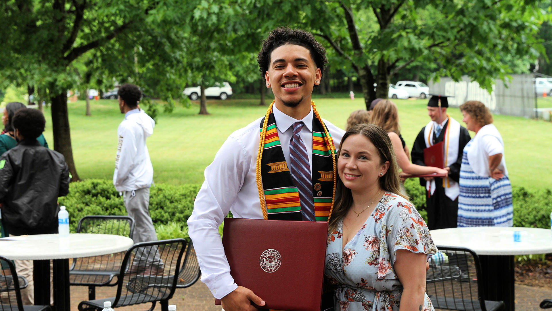 A smiling graduate takes a photo with a friend outdoors after Commencement.