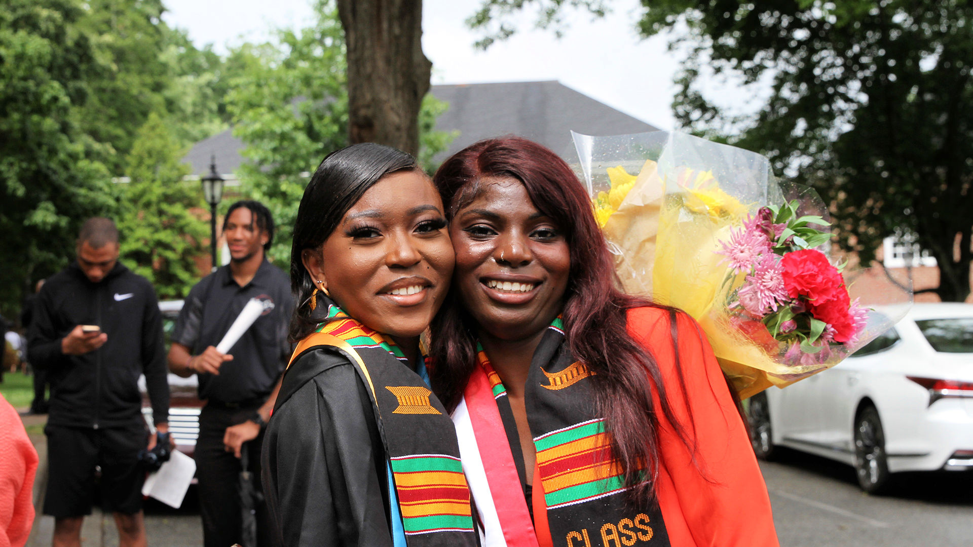 Two smiling graduates take a photo together outdoors after Commencement.