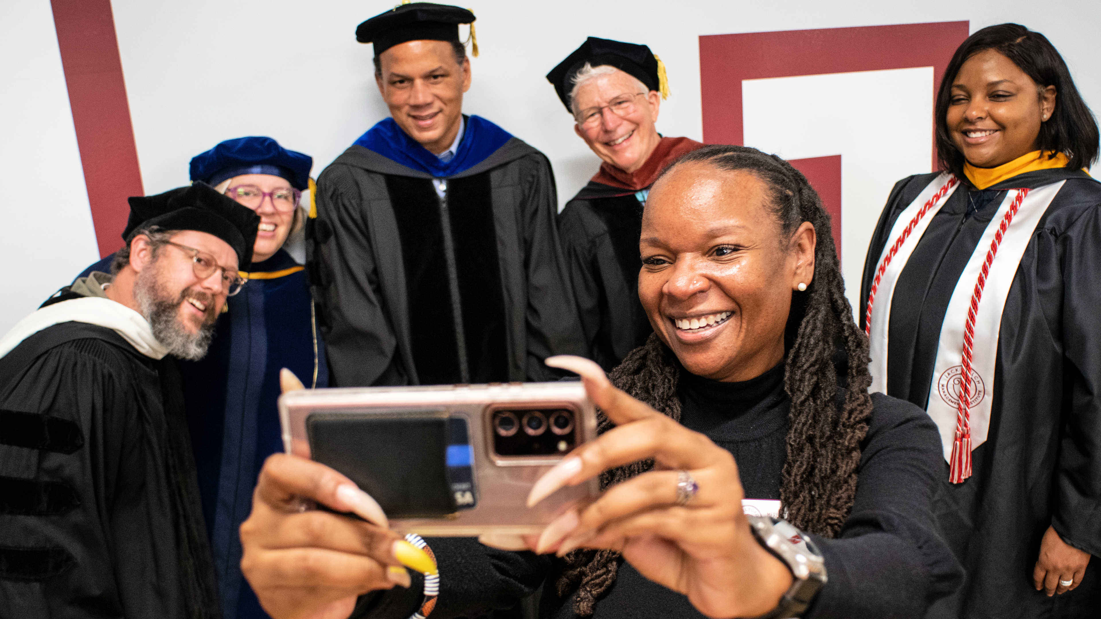 A staff member takes a selfie with a group of speakers and attendees, including the President and the Provost and the alumni speaker.