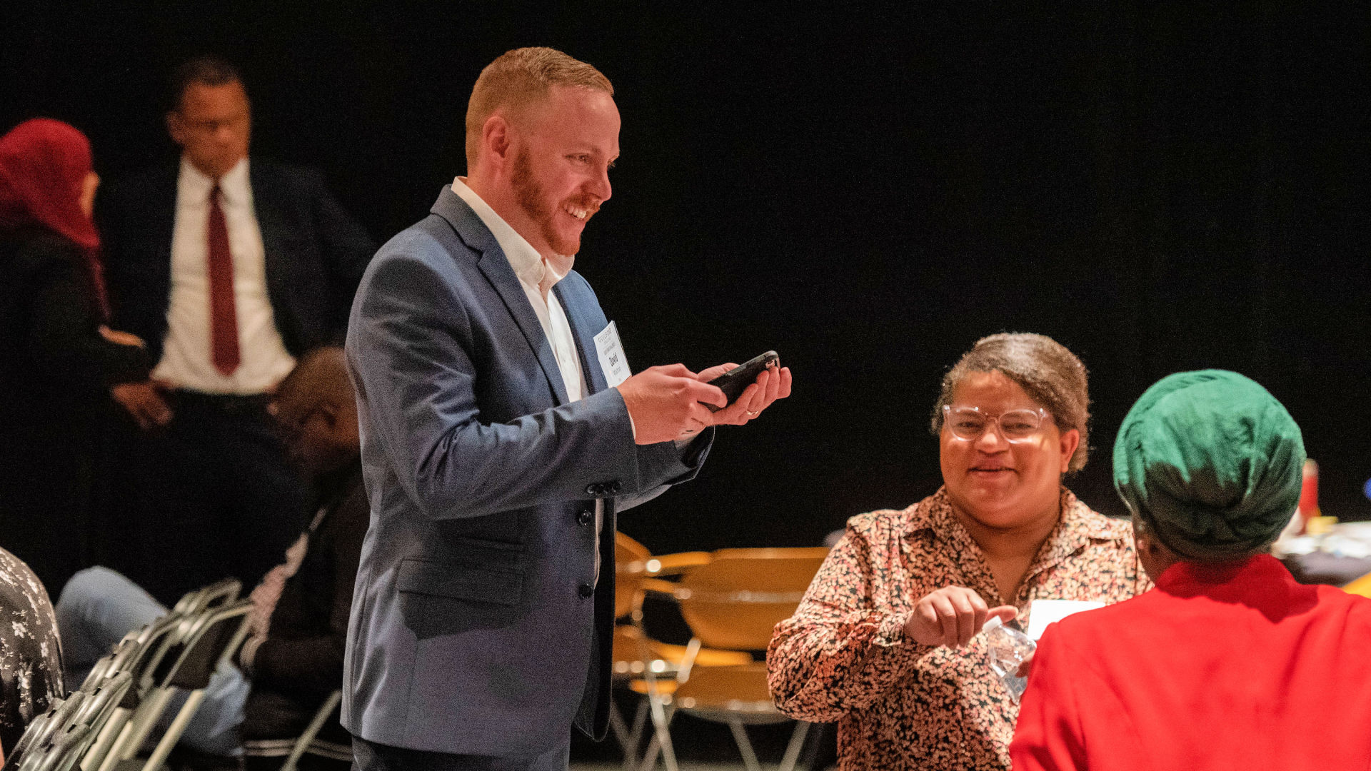 An attendee stands to chat with two other visitors at a table during the Guilford Dialogues.