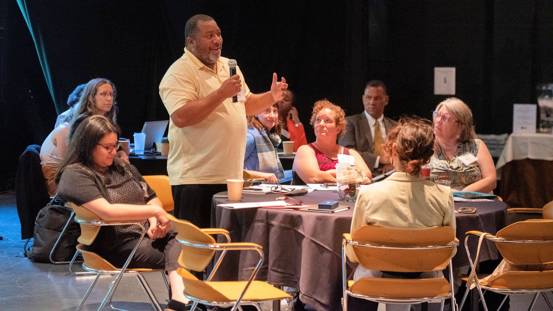 An attendee stands up near a table to ask a question during the Guilford Dialogues.