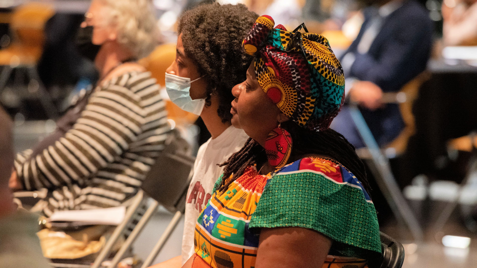 An attendee wearing a colorful, matching head wrap and outfit sits in the audience at the Guilford Dialogues.