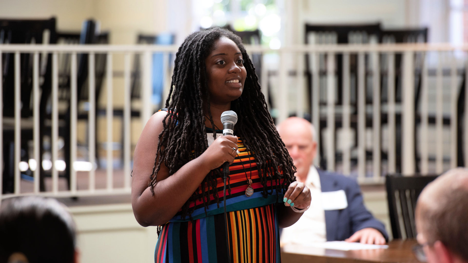 An attendee stands to speak into a handheld microphone in the Dining Hall during the Guilford Dialogues.