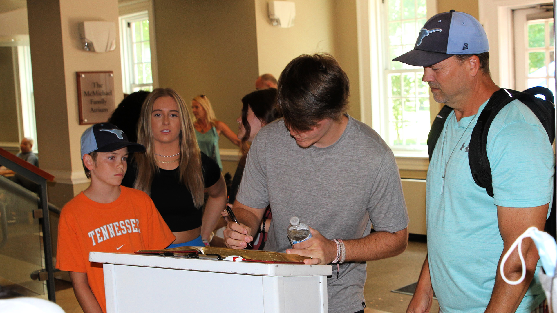 A student surrounded by family members signs the check-in book in Founders Hall on Move-in Day.