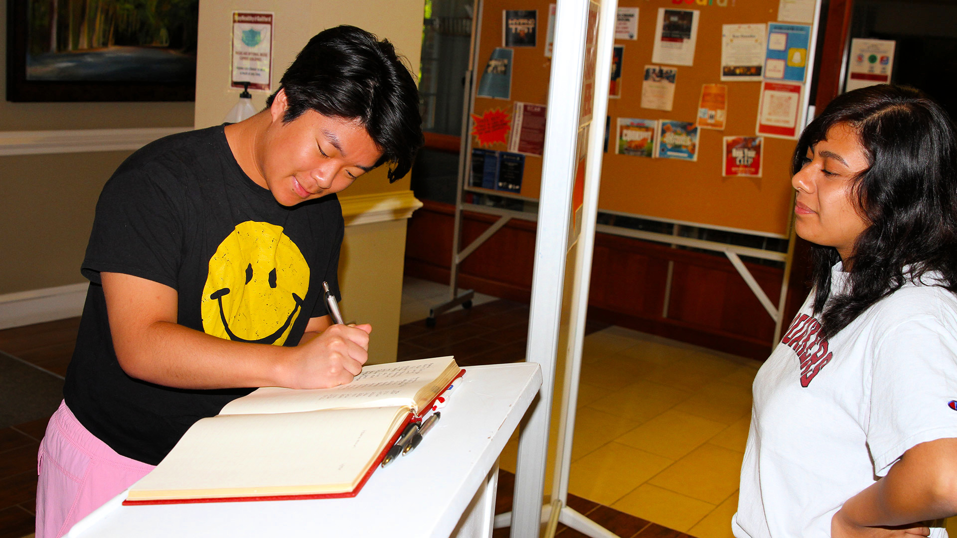 A student signs the check-in book while a current student watches in Founders Hall.