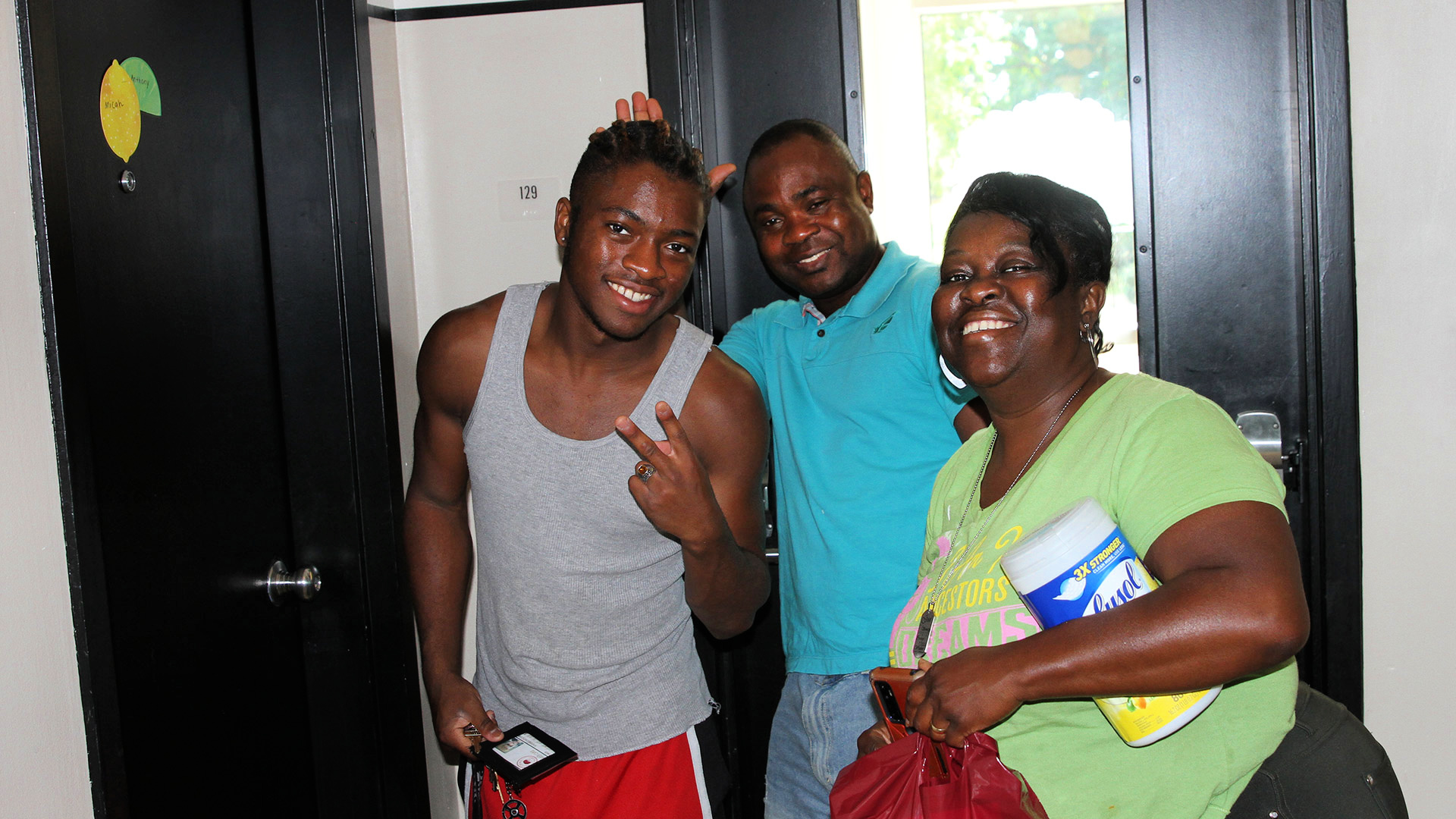 A new student takes a group photo with two smiling friends and family members as they set up the student's new room.