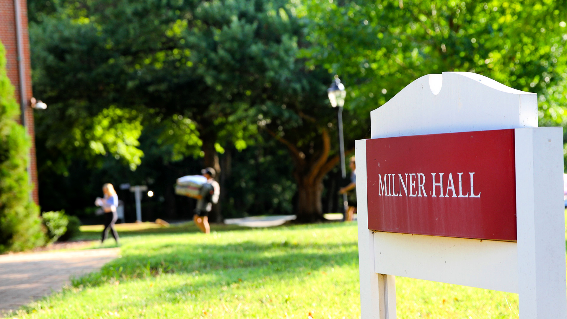 A student and friend carry items into Milner Hall, a first-year residence hall, behind the building sign.