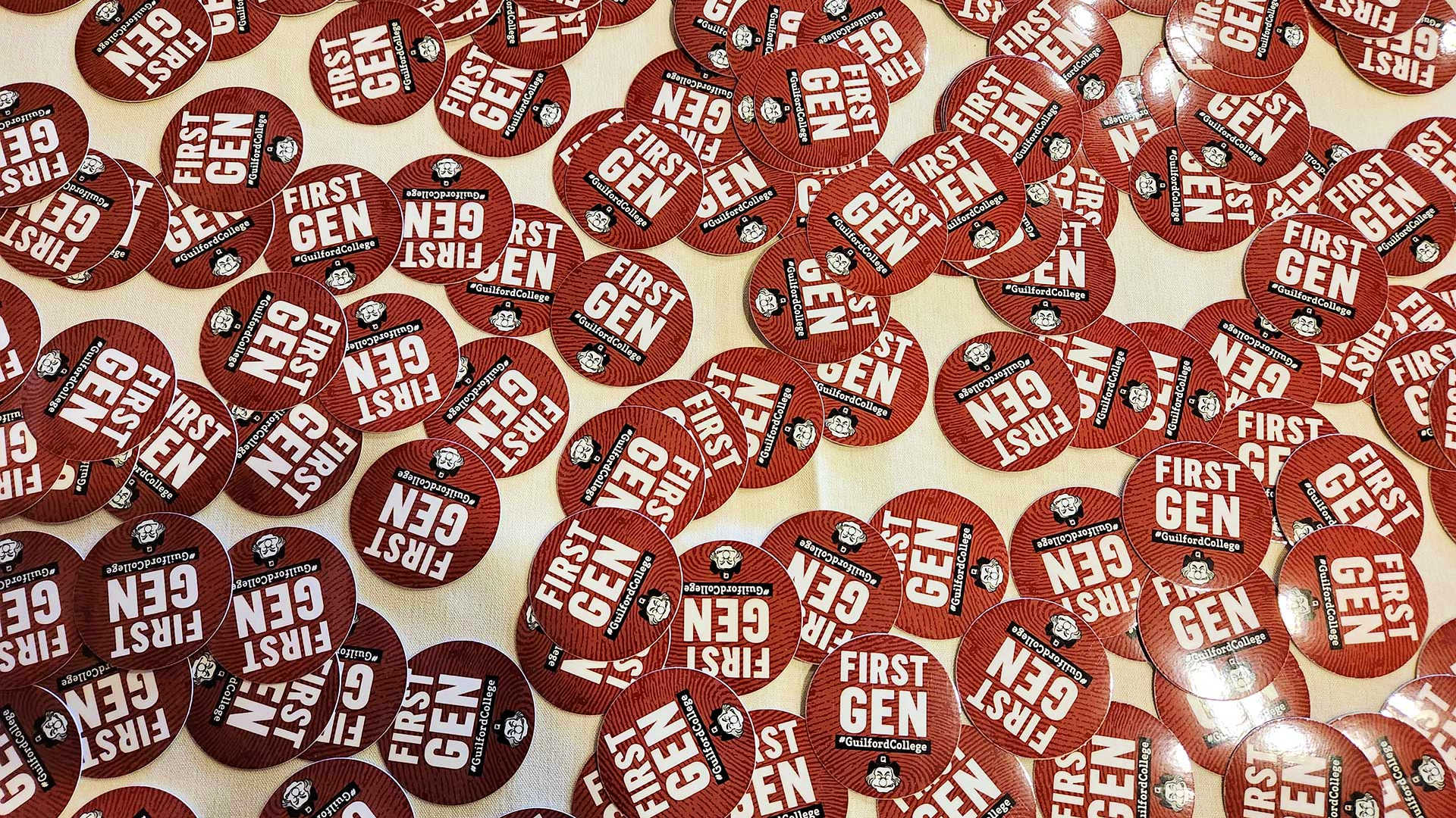 A pile of stickers that read First Gen Proud and show the Guilford College Quaker Man mascot lay on a table.