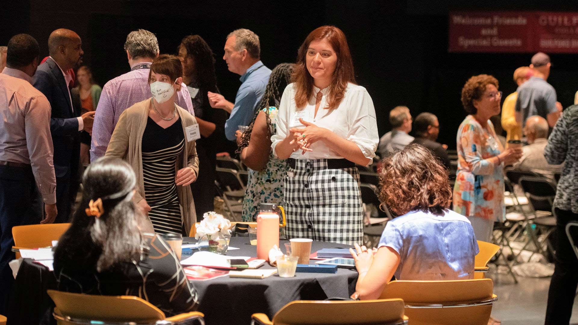 An attendees talks to other visitors seated at a table during a break in the Guilford Dialogues.