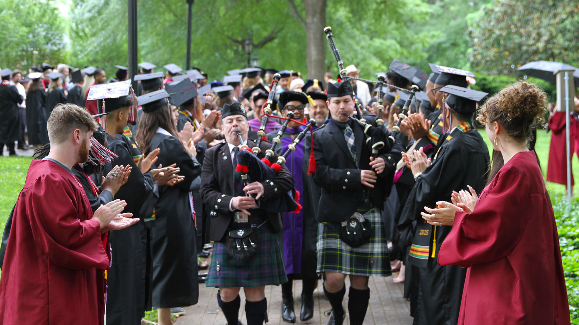 Bagpipers lead faculty members between rows of graduates and marshals.