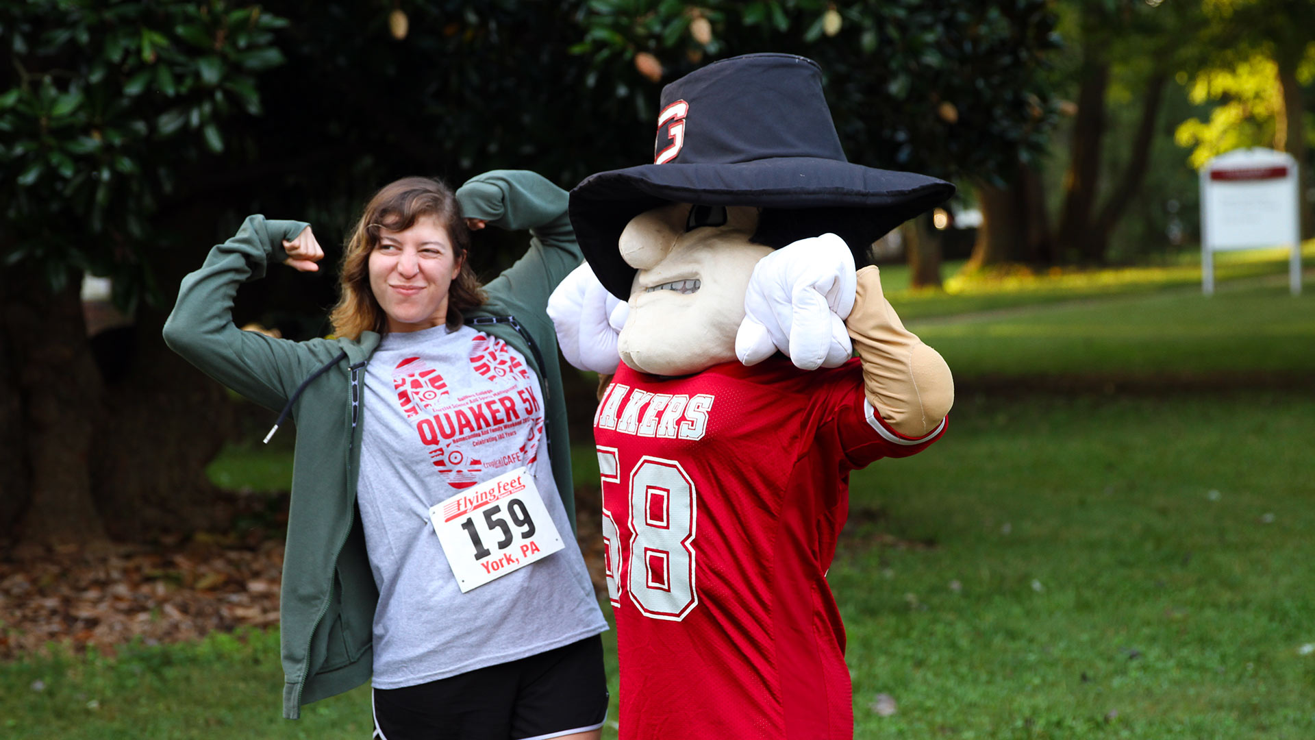 Nathan the Quaker Man mascot and a student show off their muscles at Homecoming.
