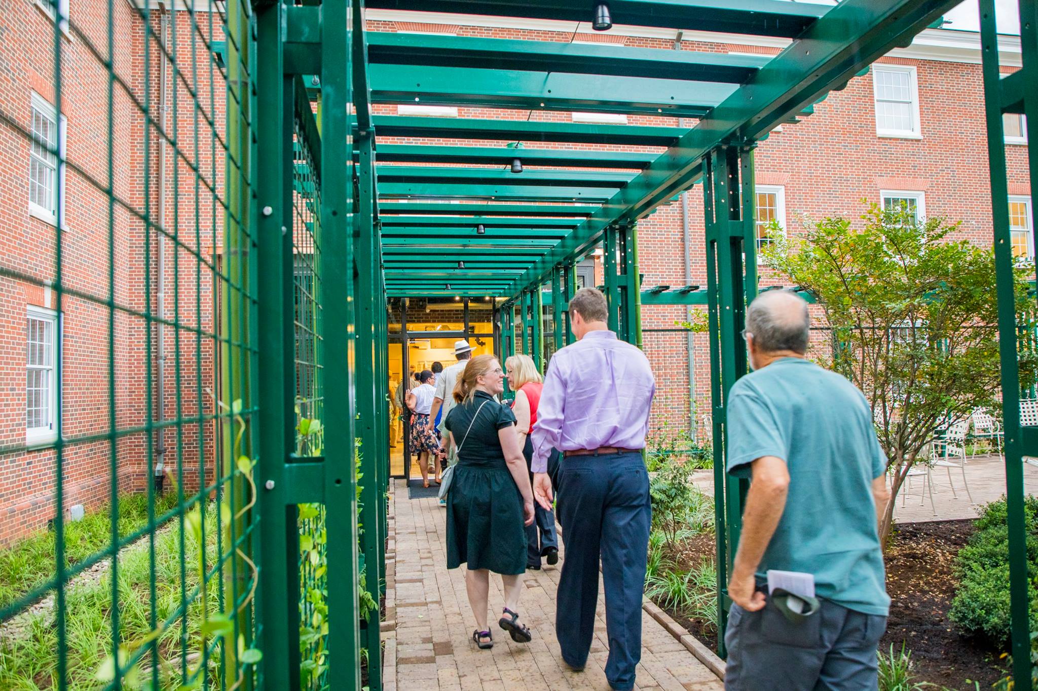 Guests walk through a path covered with a green trellis that will soon be covered in vines and flowers outside of Binford.