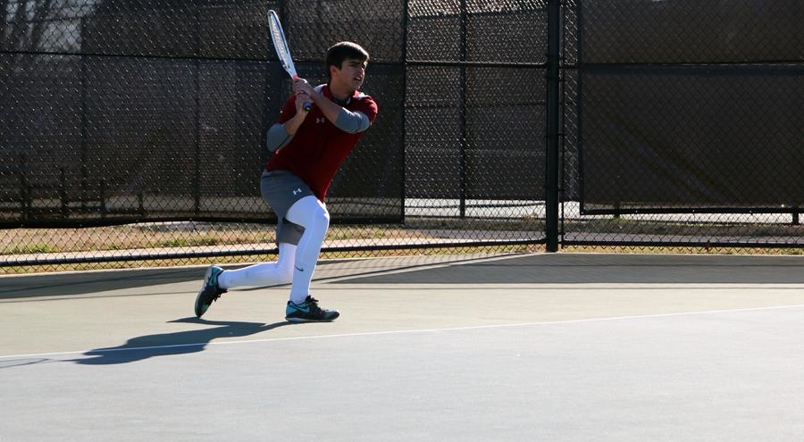 Elijah Gregory '21 swings the tennis rack on a Guilford College court.