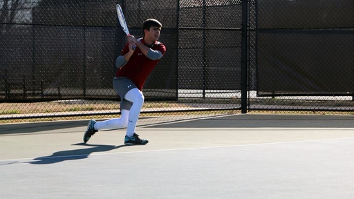 Elijah Gregory '21 swings the tennis rack on a Guilford College court.