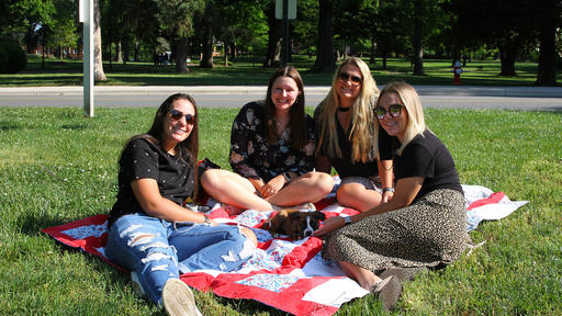 Friends sit on a blanket on the Quad with a puppy in the middle of them.