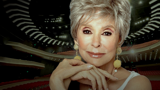 A photo of Rita Moreno wearing a white top with thin straps and round yellow drop earrings sits on a background showing the new Tanger Center auditorium.