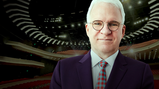 A photo of Steve Martin wearing glasses, a blue suit, white shirt, and red and blue tie sits on top of a background showing the new Tanger Center auditorium.