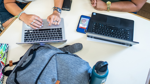 Students sit at a table with their laptops open, preparing to type.