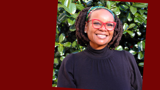 Photo of Meredeth standing outdoors wearing a long-sleeve black top, red glasses, and multicolored head band