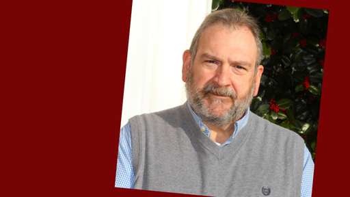 John stands outside wearing a long sleeve blue button down shirt with a gray vest over it.