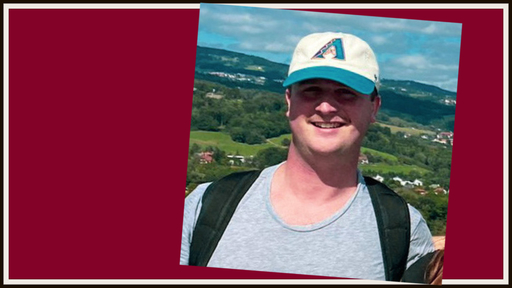 Ian Stafford '18 stands outside wearing a gray tee, a backpack, and a baseball cap.