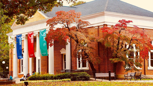 Trees filled with fall colored leaves surround Guilford's Hege Library as students sit on the front steps.