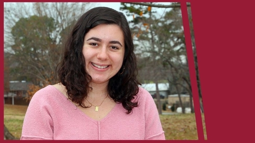 Jenni Camhi' 22 stands outdoors on Guilford's campus, wearing a pink sweater and a necklace.