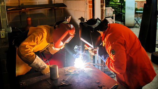 A faculty member and a student wearing safety gear work on a welding project together.