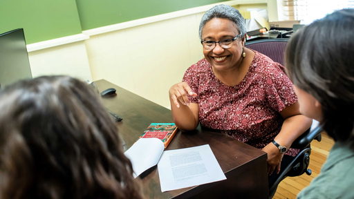A faculty member talks to two students in their office.