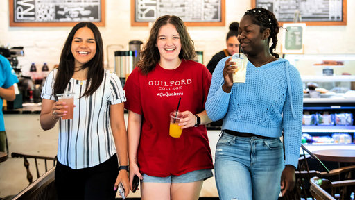 Three students laugh as they carry their drinks out of Rachel's Rose Cottage.