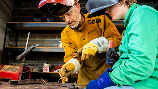 A faculty member explains a welding technique to a student.