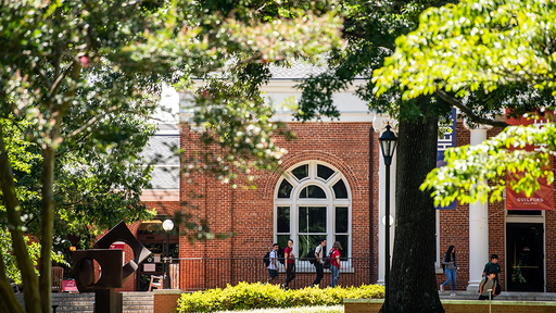 A group of students walk across the front porch of Hege Academic Commons.