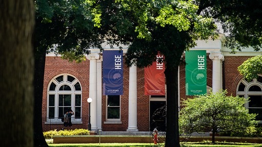 The front of Hege Academic Commons is seen through the trees on the Quad.